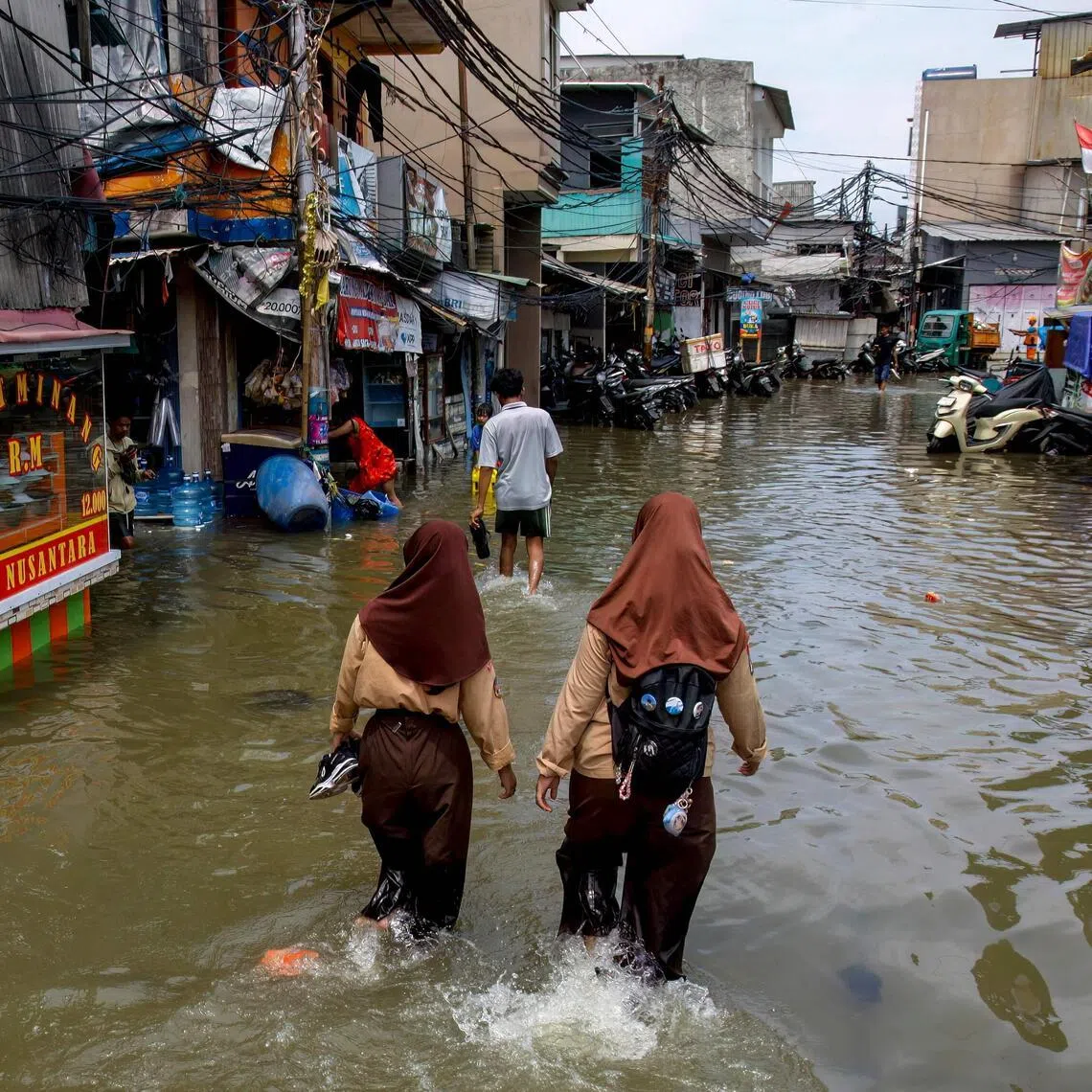 Two schoolgirls wade through a street flooded by high tide in Muara Baru, Jakarta on Dec 6, 2025.