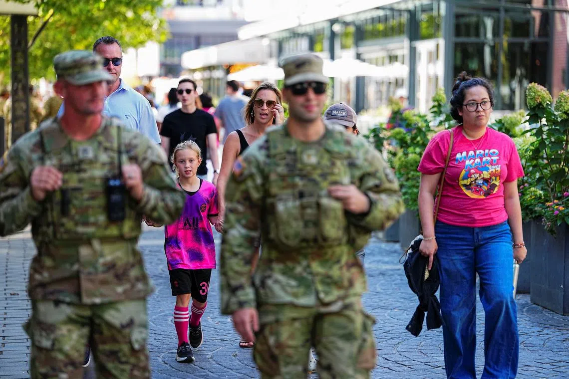 People walk on the street near members of the National Guard after U.S. President Donald Trump deployed the National Guard and ordered an increased presence of federal law enforcement to assist in crime prevention, in Washington, D.C., U.S., August 23, 2025. REUTERS/Aaron Schwartz/File Photo