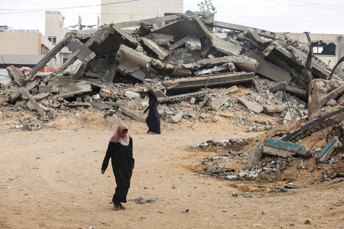 Palestinian women walk near rubble after a ceasefire, in Khan Younis in the southern Gaza Strip, October 9. REUTERS/Ramadan Abed