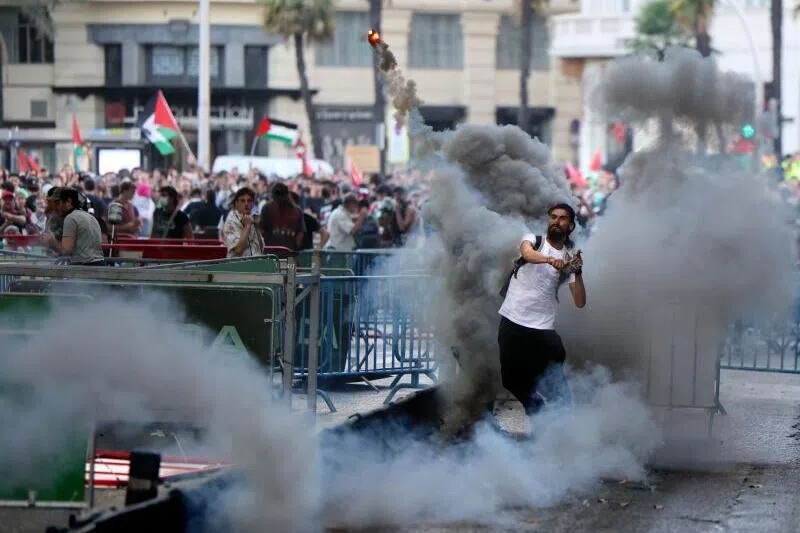 A man throws a smoke flare back at police after Pro-Palestinians protestors invaded the street forcing race organisers to abandon the 21st and final stage of the Vuelta a Espana 2025, in Madrid.
