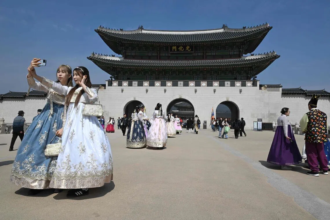 This picture taken on March 16, 2026 shows visitors wearing traditional hanbok dresses taking a selfie in front Gwanghwamun Gate, the main gate of Gyeongbokgung Palace, in Seoul. The world's biggest boy band is set for a comeback concert on March 21, after a nearly four-year hiatus for the septet to do military service -- and while the nation went through traumatic times. (Photo by Jung Yeon-je / AFP) / TO GO WITH AFP STORY, SKorea-entertainment-music-BTS-politics,  FOCUS by Claire LEE