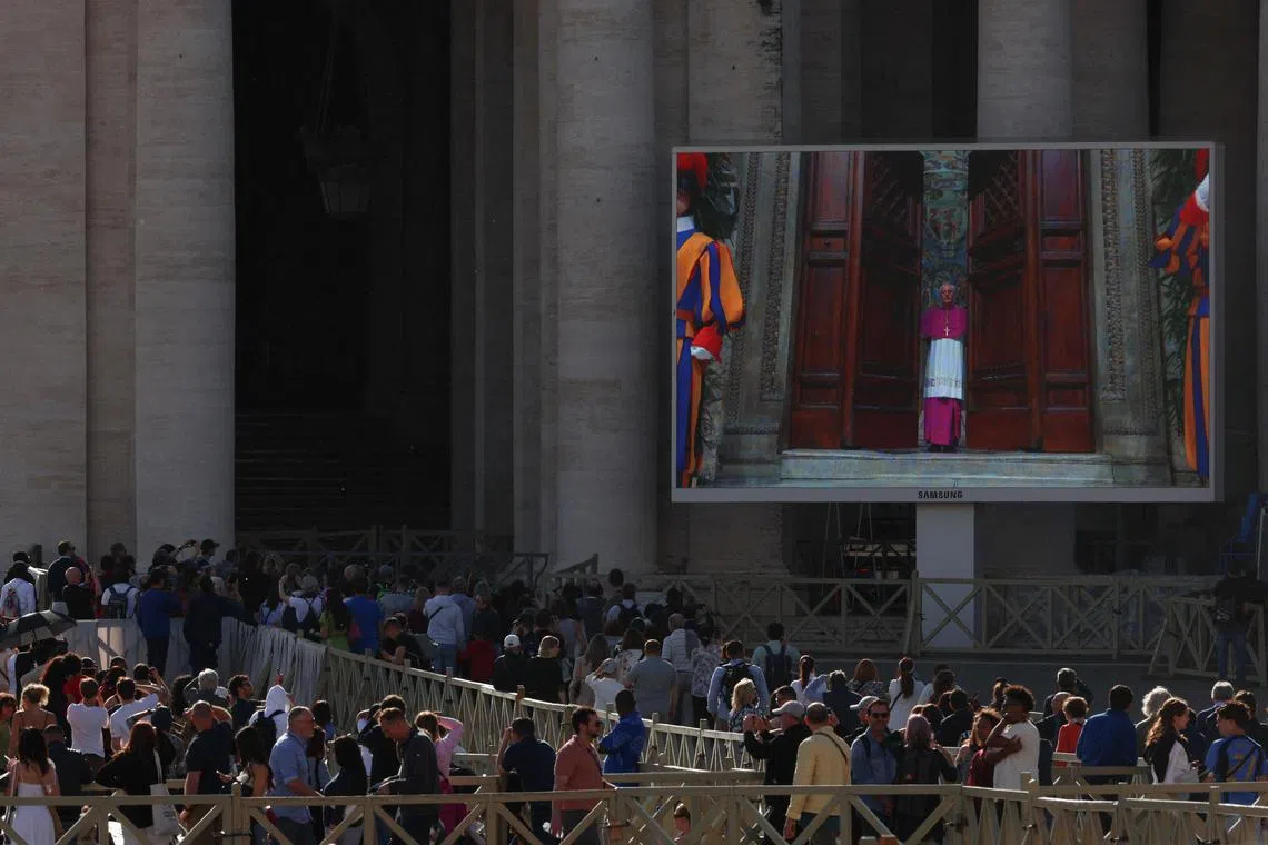 People watching at the Vatican on May 7, as a screen shows a clergy member closing the door to the Sistine Chapel, on the first day of the conclave to elect a new pope.