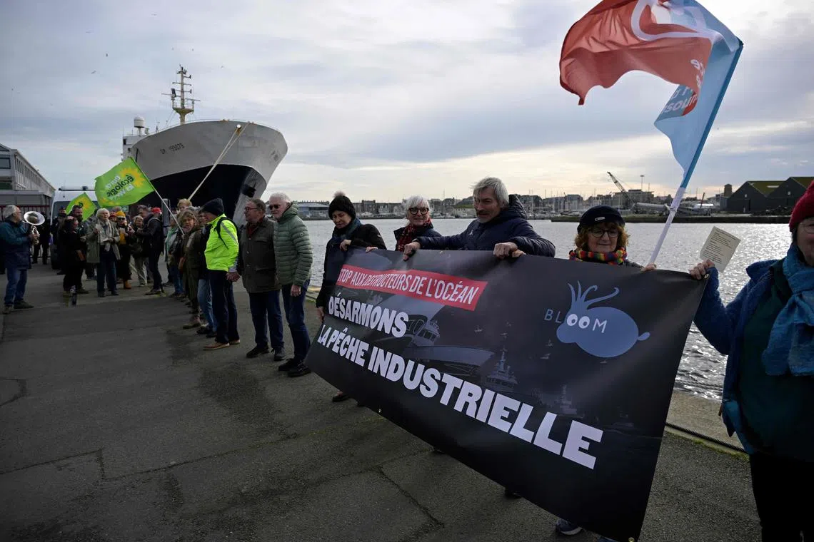 People join hands at the Saint-Malo protest and hold a banner in French, reading  "Stop destroyers of the ocean, let's disarm industrial fishing".