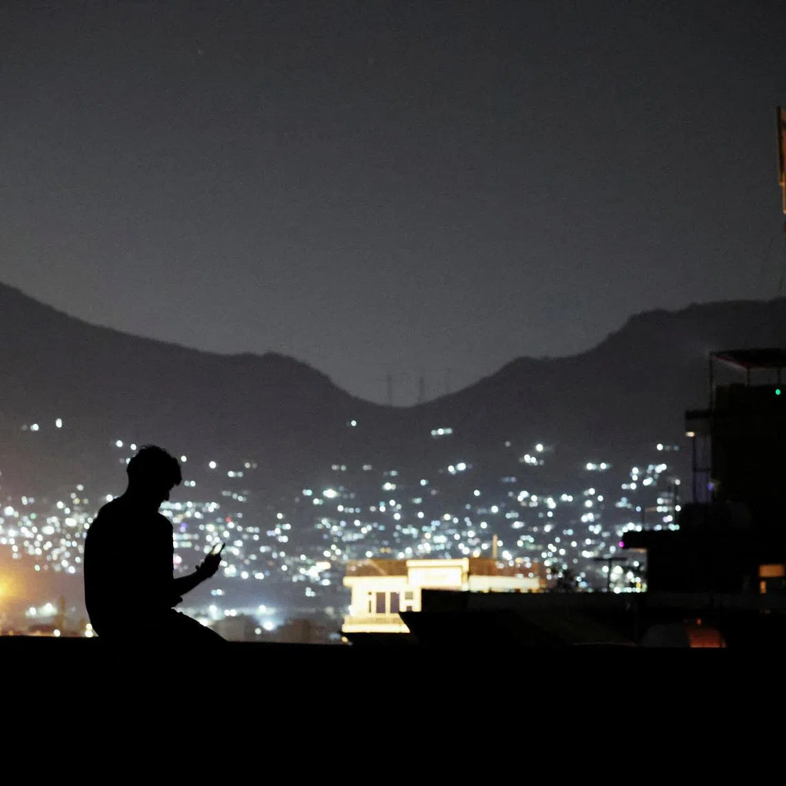 FILE PHOTO: A man sits on a wall while talking to someone on a video call in Kabul, Afghanistan, October 1, 2025. REUTERS/Sayed Hassib/File Photo