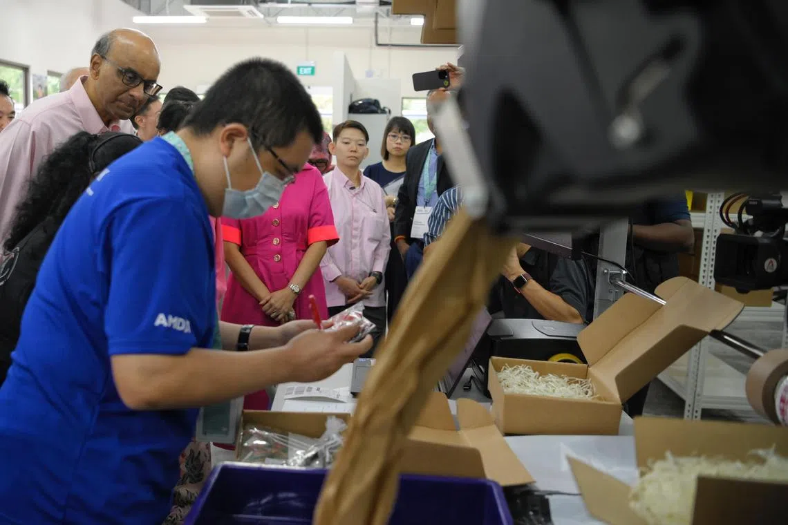 President Tharman Shanmugaratnam (left) watches as Bizlink Centre Singapore trainee Chan Yong Shen (foreground), 38, packs parcels at the Enabling Business Hub (EBH) during the opening ceremony on December 13, 2023.