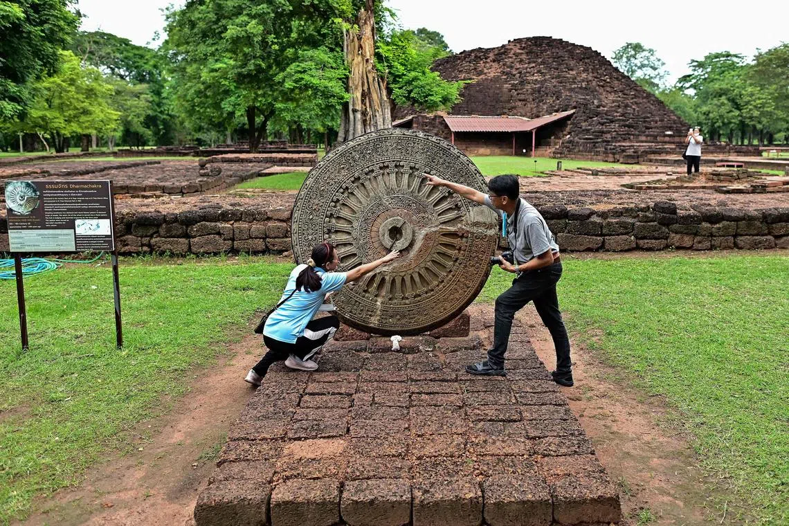 Tourists looking at an ancient Dharmachakra artefact at the Si Thep historical site in Thailand.