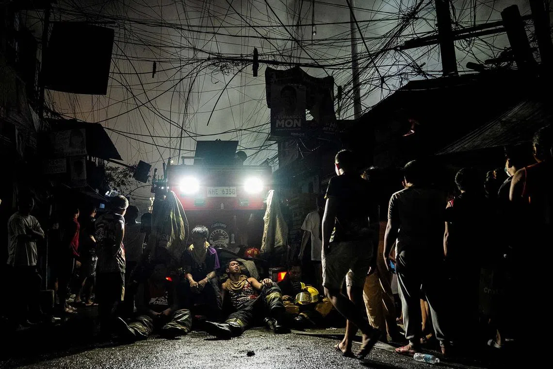 Firefighters taking a break next to residents watching a fire at a residential area in Manila, Philippines, April 23, 2025. 