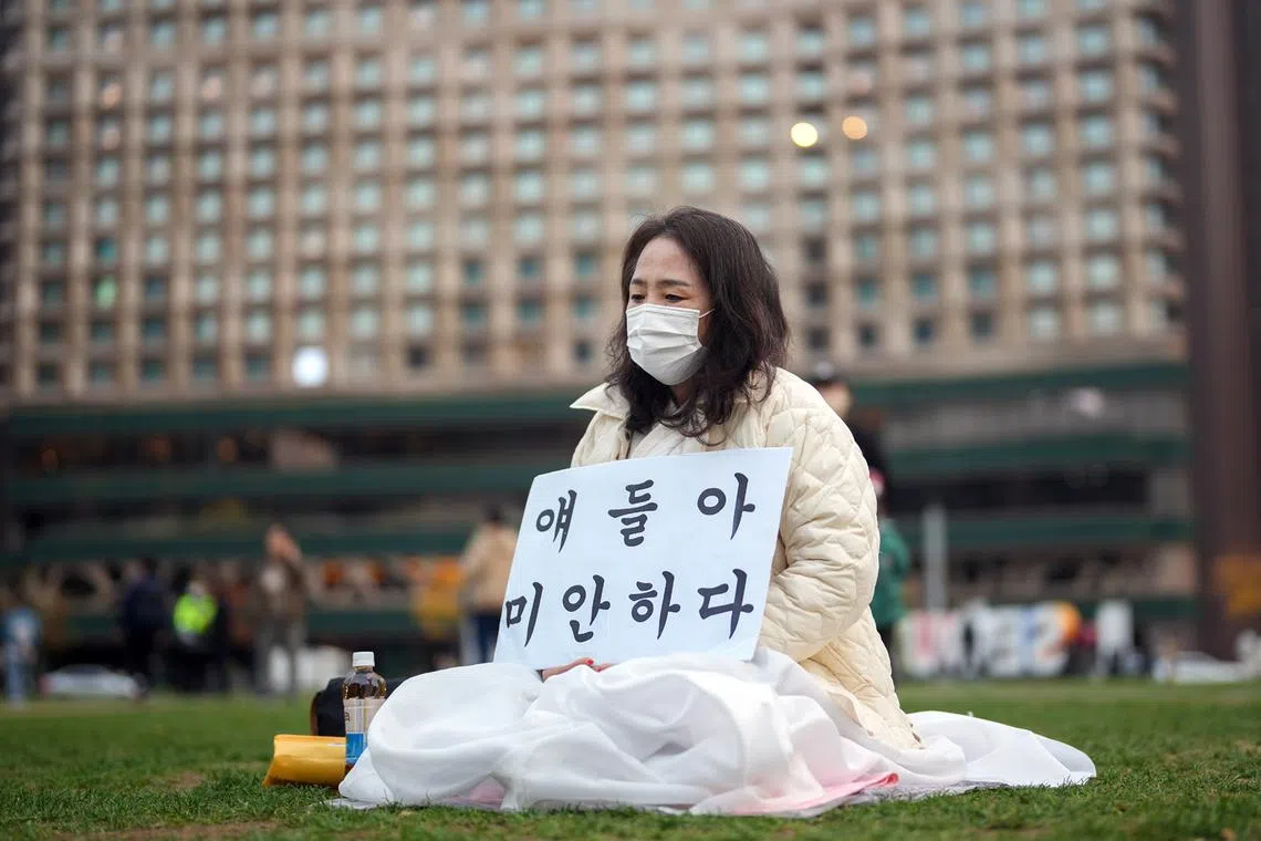 Lee In-sook, 62, holds a sign reading 'Children, I am sorry' as she sits outside the Samsung Seoul Funeral Home in Seoul, South Korea, Oct. 31, 2022. 