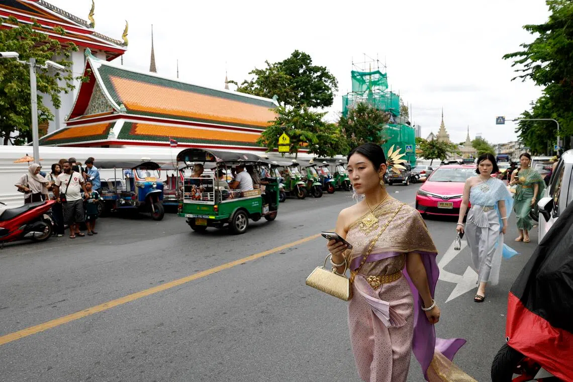 Foreign tourists wearing Thai traditional costumes walk at a tourist spot outside Wat Pho Temple, or the Temple of the Reclining Buddha in Bangkok.