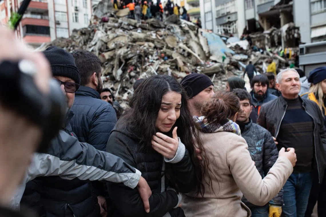 A woman reacts as rescuers search for survivors through the rubble of collapsed buildings in Adana, on Feb 6, 2023, after a 7.8 magnitude earthquake struck the country's south-east. 
