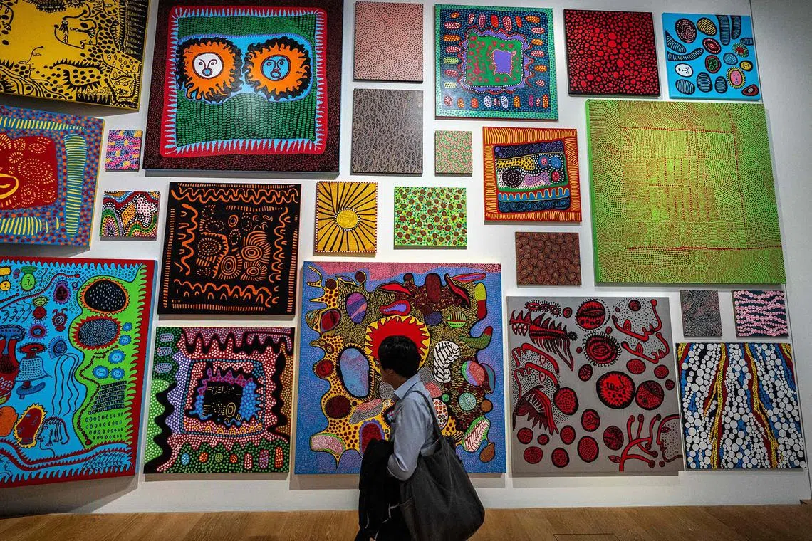 A member of the press walks past a wall presenting works by Japanese artist Yayoi Kusama during the media preview of the exhibition "I would overcome death and go on living" at Yayoi Kusama Museum in Tokyo on October 16, 2024. (Photo by Philip FONG / AFP) / RESTRICTED TO EDITORIAL USE - MANDATORY MENTION OF THE ARTIST UPON PUBLICATION - TO ILLUSTRATE THE EVENT AS SPECIFIED IN THE CAPTION
