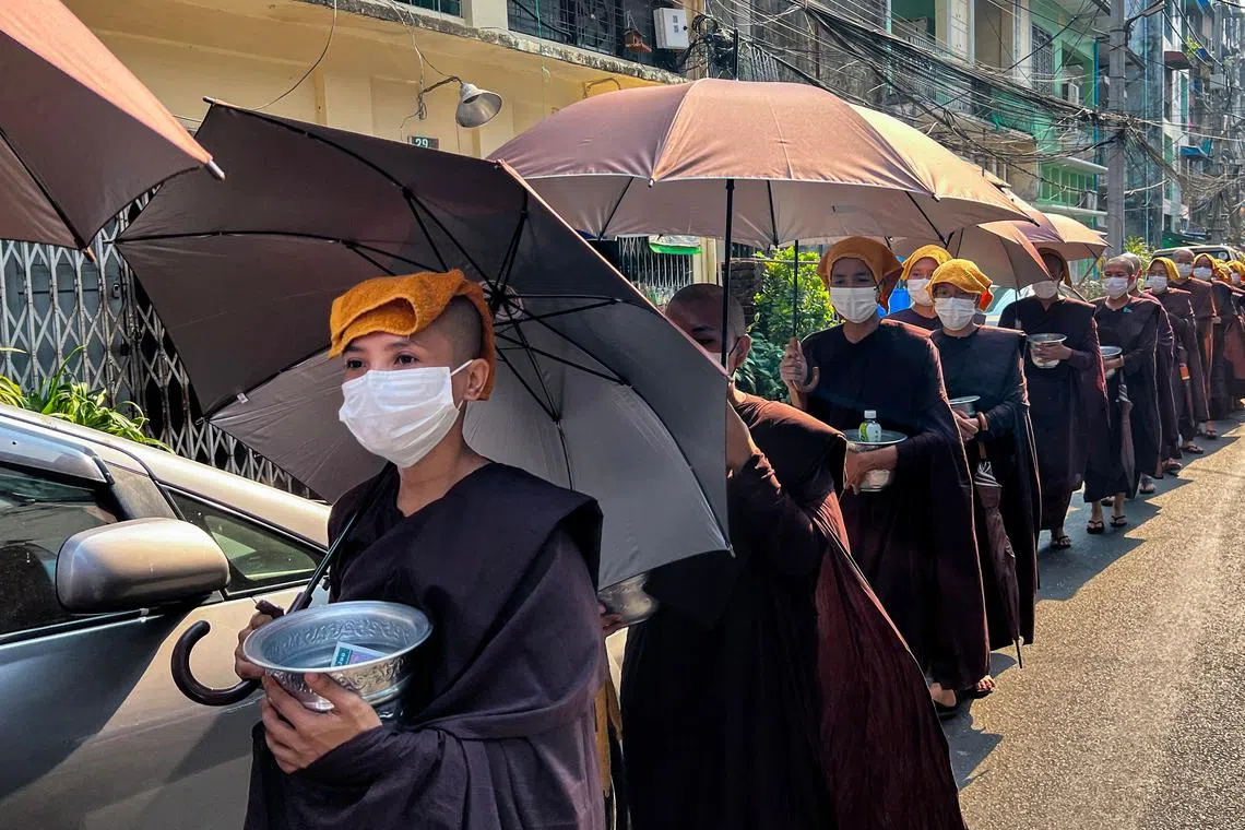Buddhist nuns collect alms with their head covered with towels and under umbrellas to shelter from the sun during a heatwave in Yangon on April 24, 2023. 