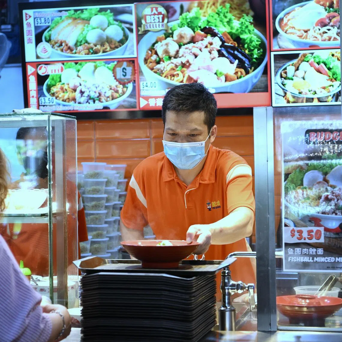 A hawker at a stall with the budget meal sticker serving up a bowl of teochew noodles.