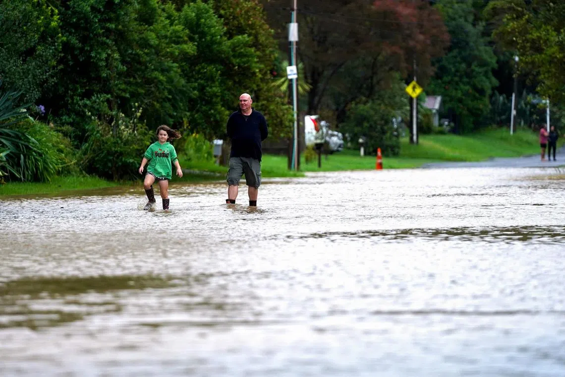 Residents wade through a flooded street after torrential rain at the suburb of Langholm in Auckland on February 1, 2023. (Photo by Diego Opatowski / AFP)