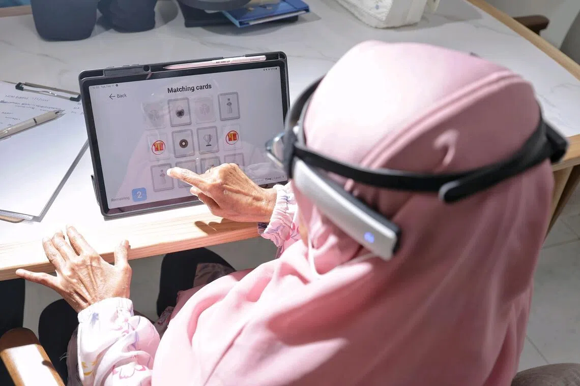 Madam Rupiah Sarwan, 78, playing games on the tablet as part of cognitive therapy at home on Feb 11, 2025. The headband evaluates her brain function.