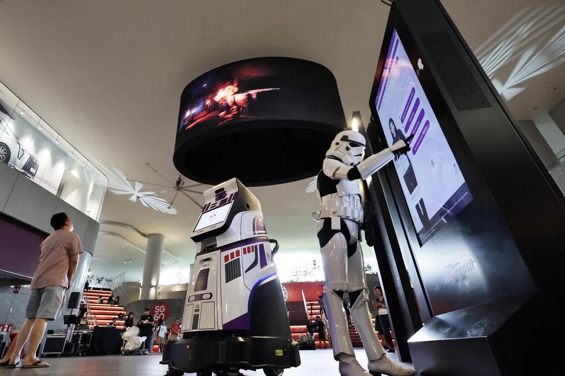 At the heart of the Digital Village is the (top)Spectacular Screen ? a 6m-wide, 2.5m-high elliptical LED displaywhich is so named as it offers an immersive cinematic experience with stunning 3D visuals that vividly 
come to life. A first in a public transport hub, the Spectacular Screen is located at the amphitheatre which brings people together and supports digital showcases, performances, talks, and exhibitions and the (far R)AIVA digital concierge by transport operator SBS Transit, the AI Virtual Assistant, that helps commuters with journey planning and wayfinding. She is accompanied by (center)MR-2, a robot 
with multi-role capabilities, to perform safety, security, and cleaning duties independently. 
These digital innovations embody the essence of the Punggol Digital Village, showcasing howtechnology can enable smarter, safer, and more delightful commutes.