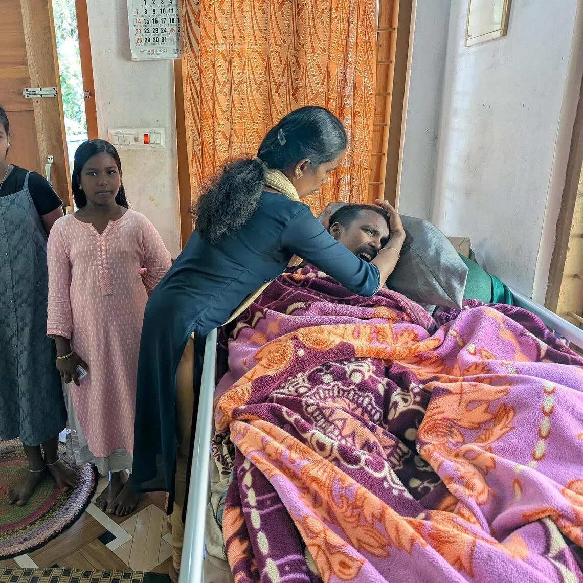 Mrs Parameshwari S. fixes her paralysed husband Selvam's pillow as her daughters look on. The family was listed as extremely poor in a Kerala state programme.