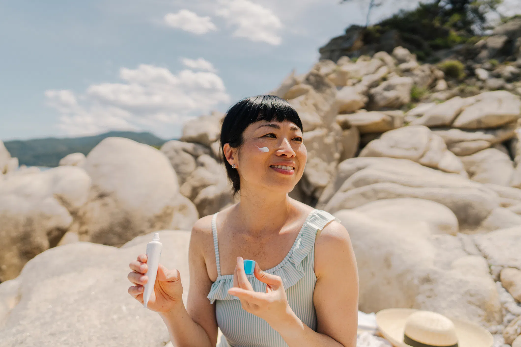 Best 9.9 sales in Singapore for beauty and skincare deals: Woman applying sunscreen on her face while at the beach