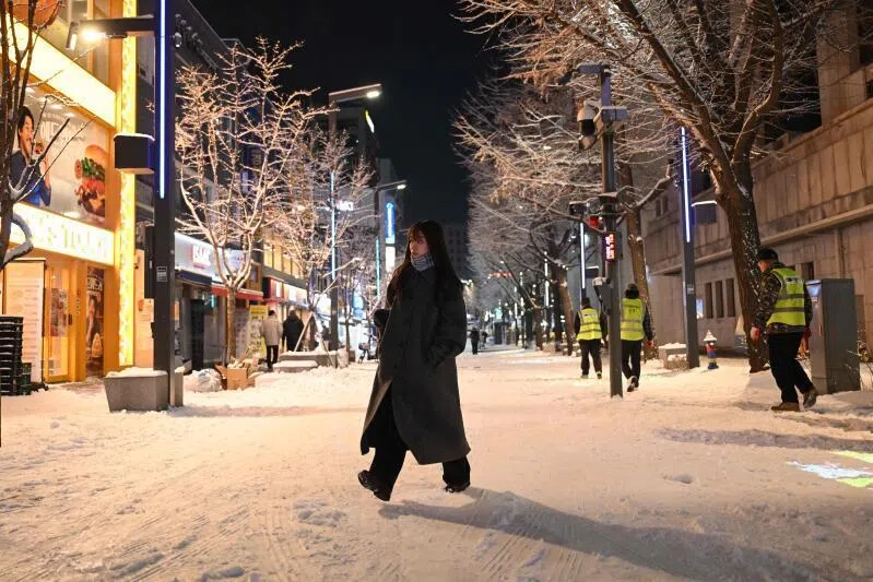 Pedestrians walk on a snowy street as the season's first snow falls in downtown Seoul on Dec 4.