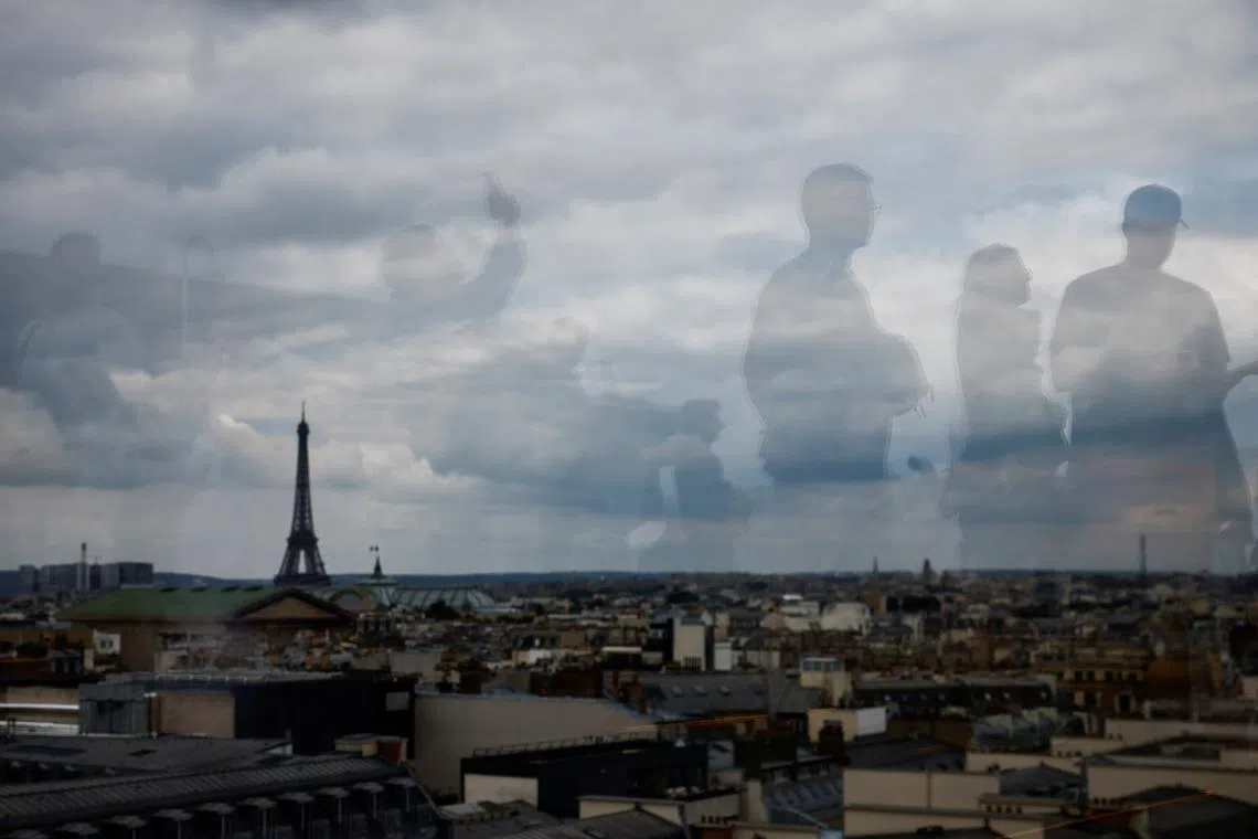 Tourists are reflected on the balustrade as they look at the Eiffel Tower and the Paris skyline from the rooftop of the Galeries Lafayette department store on a cloudy day in Paris, France, July 1, 2024. REUTERS/Yara Nardi/File Photo