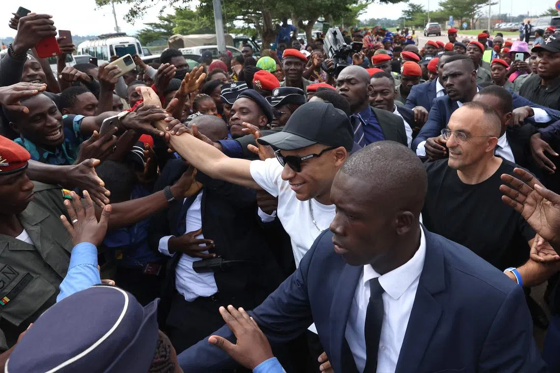 PSG striker Kylian Mbappe (centre) greets crowds gathered outside Yaounde airport.