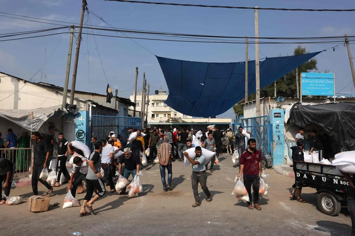 Palestinians collect bags of dried pulses from a UN-run aid supply center in Deir al-Balah, on Oct 28, 2023.