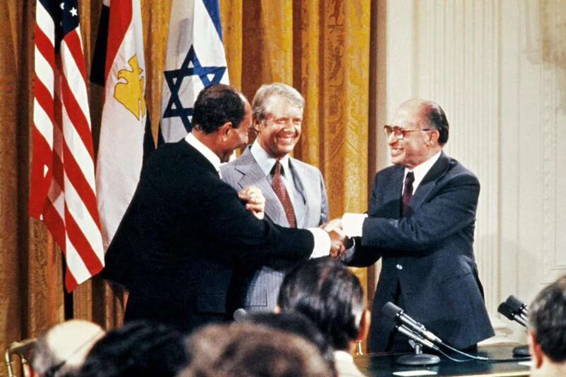 (FILES) Egyptian President Anwar al-Sadat (L), Israeli Premier Menachem Begin (R) and US President Jimmy Carter (C) shake hands after a press conference in the East Room of the White House, on September 18, 1978.i to Egypt. Jimmy Carter holds a unique place in US politics: he is the oldest former president and a Nobel peace laureate, who left office under a cloud of unpopularity and has seen his star rise ever since. (Photo by FILES-CONSOLIDATED NEWS PICTURES / AFP)