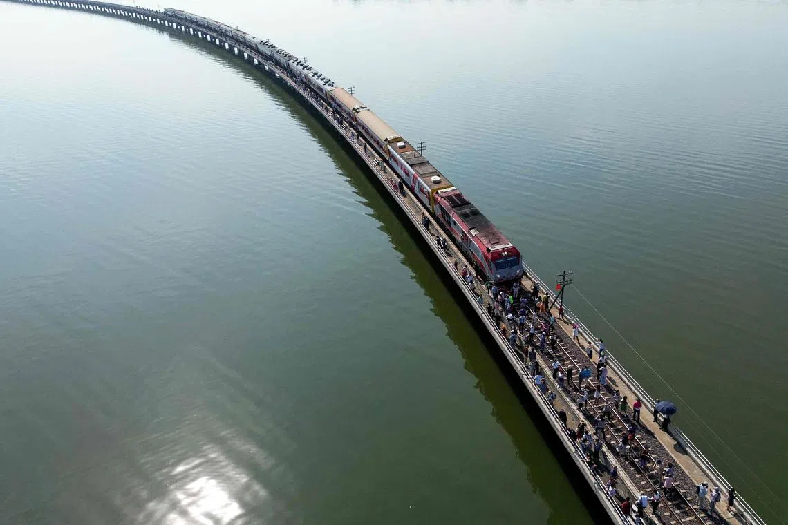 This aerial photograph taken on November 4, 2023 shows tourists travelling aboard the popular "Floating train" taking photographs along the railway tracks during a stop in the middle of Pasak Jolasid Dam, Thailand’s biggest reservoir in Lopburi province. A lone boatman watched the spectacle of Thailand's so-called "floating train" as selfie-seeking passengers soaked up the water views after disembarking from carriages stopped on a narrow bridge. (Photo by MANAN VATSYAYANA / AFP) / TO GO WITH "THAILAND-LIFESTYLE-TRANSPORT-TOURISM" SCENE BY LISA MARTIN