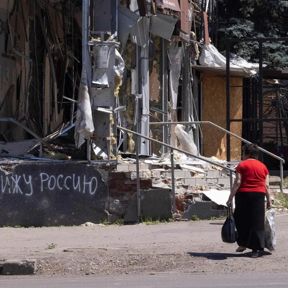 A resident of Kramatorsk, in eastern Ukraine, walks past a building destroyed by a Russian air strike with writing on the wall that reads "I hate Russia", on June 8.