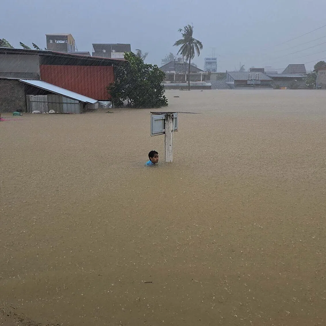 A man clinging to a street sign on a flooded street after being swept there while going out to get food supplies in Hat Yai district, which has been affected by heavy rainfall that has hit 10 provinces in southern Thailand and killed several people, in Songkhla province, Thailand, Nov 24, 2025. 