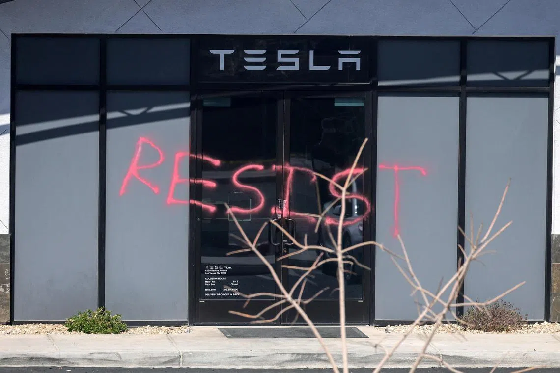 The word "Resist" is shown spray painted on the entrance of a Tesla Collision Center.