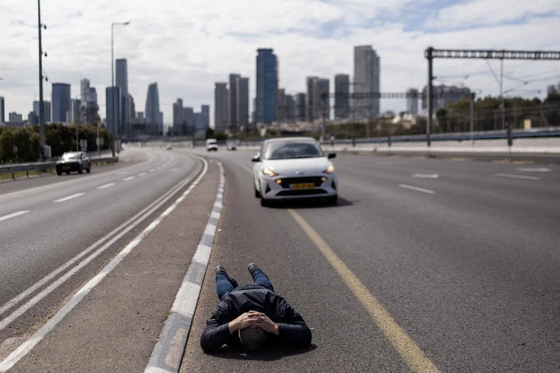 A man lies on the road to take cover as an air raid siren sounds following a barrage of missiles from Iran, amid the US-Israel conflict with Iran, in central Israel, March 9, 2026.