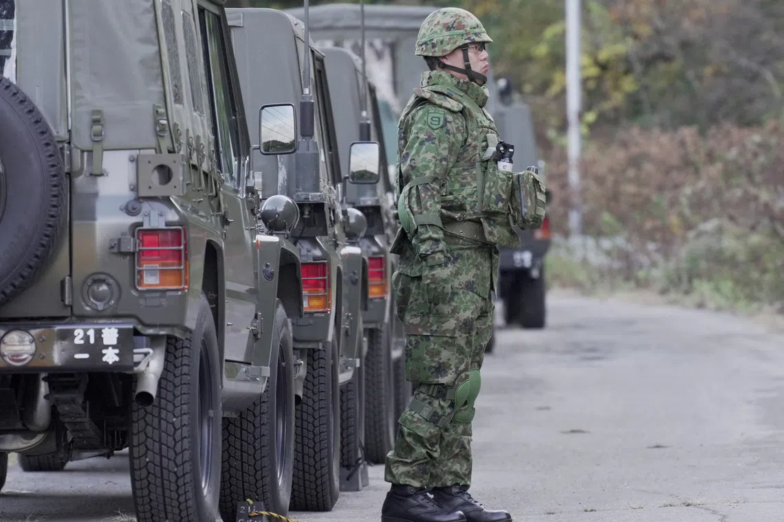 A member of Japan Self-Defence Forces stands next to military vehicles during a practice setting up a bear trap in Kazuno, Akita prefecture, Japan.