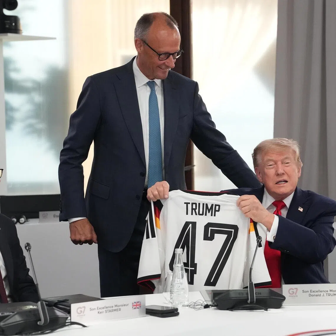 German Chancellor Friedrich Merz presents US President Donald Trump with a jersey with the number 47 on it as British Prime Minister Keir Starmer looks on.
