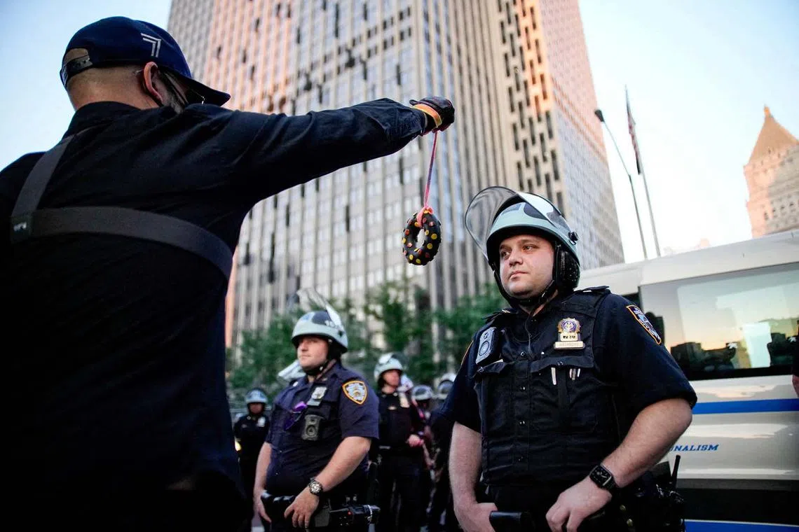A demonstrator trying to provoke a law enforcement officer with a toy donut as they detain demonstrators during a protest against federal immigration sweeps next to the US immigration court in New York City, US, June 11, 2025. 