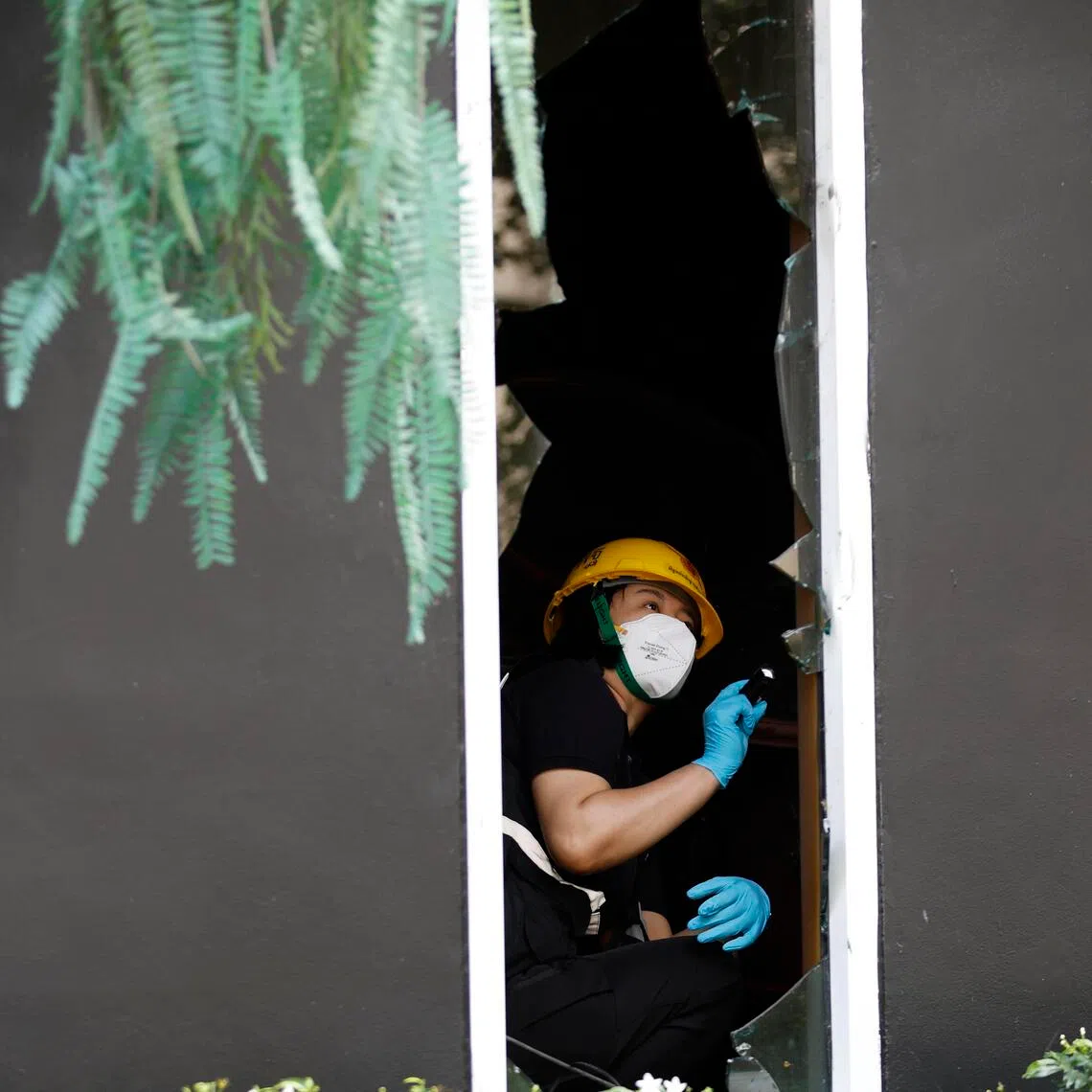 A forensic police officer examining a broken window at the scene of a fatal blaze at a pub in Bangkok on July 13.