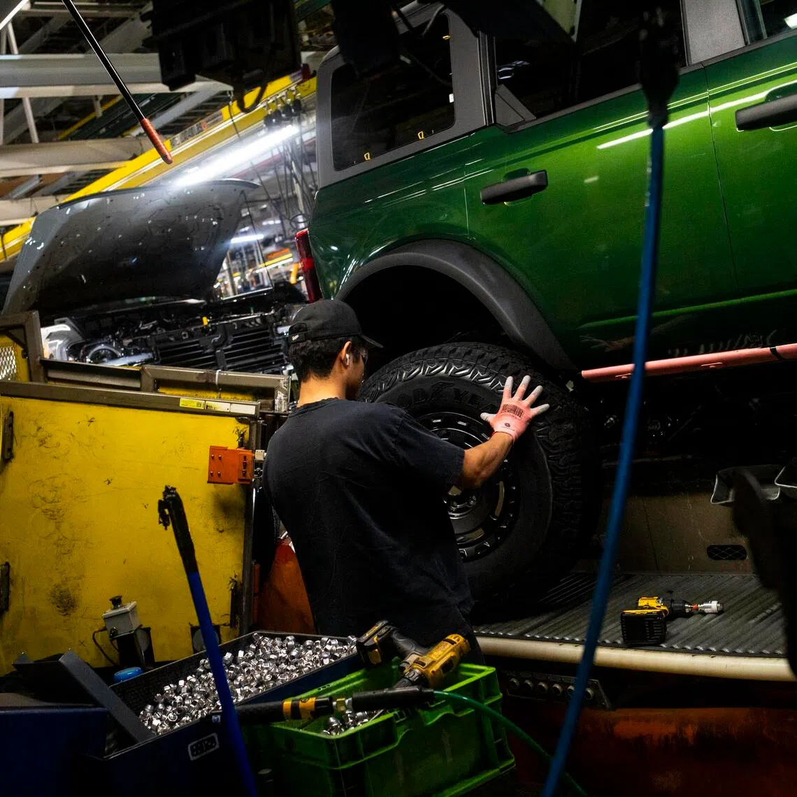 A worker fits a wheel onto a Ford Bronco at the automaker's plant in Wayne, Mich.  US automakers are facing difficult choices.
