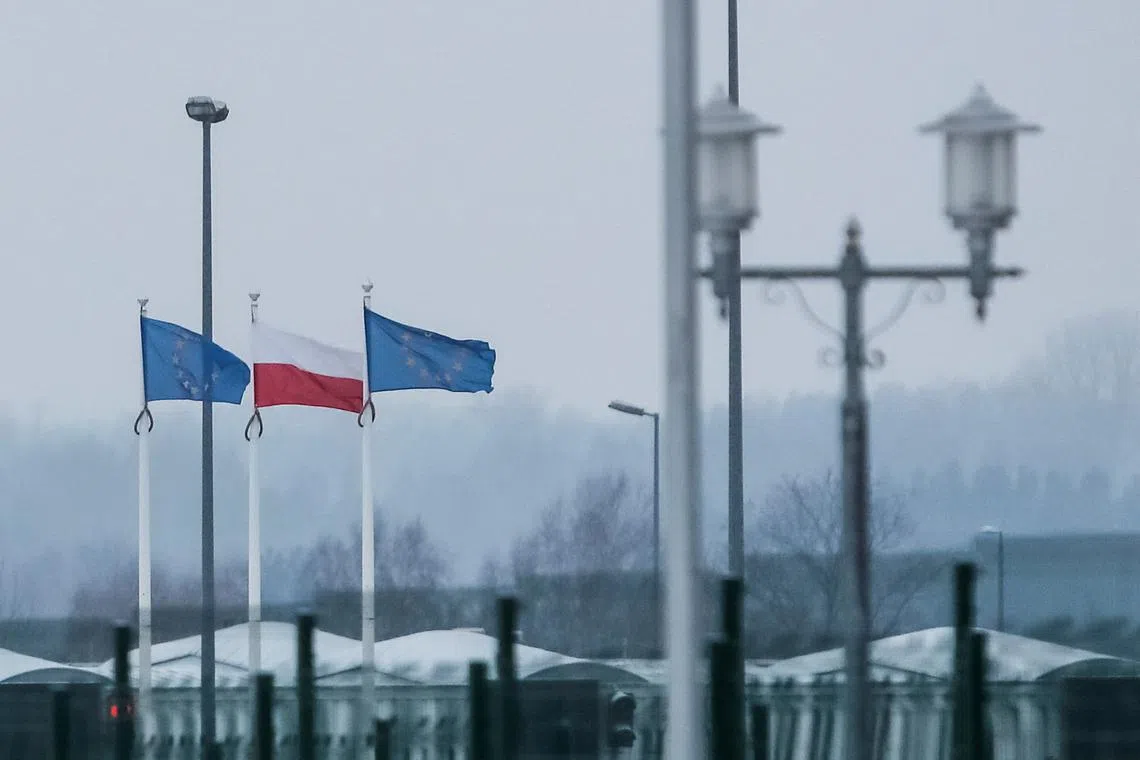 A view from the Belarusian side of the frontier shows Polish and EU flags behind a fence at Bruzgi-Kuznica checkpoint on the Belarusian-Polish border amid the migrant crisis in the Grodno region, Belarus, December 23, 2021. REUTERS/Maxim Shemetov/File Photo