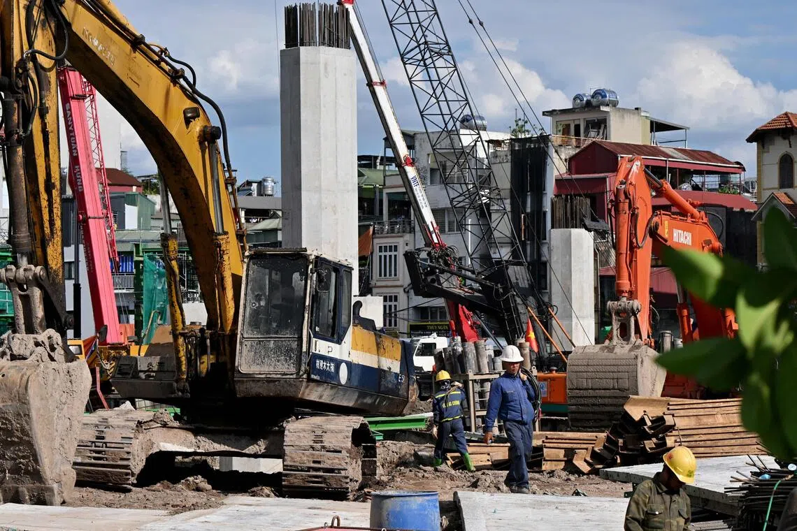 Workers walk past excavators at the construction site of the Tran Hung Dao Bridge, spanning across the Red River in Hanoi.