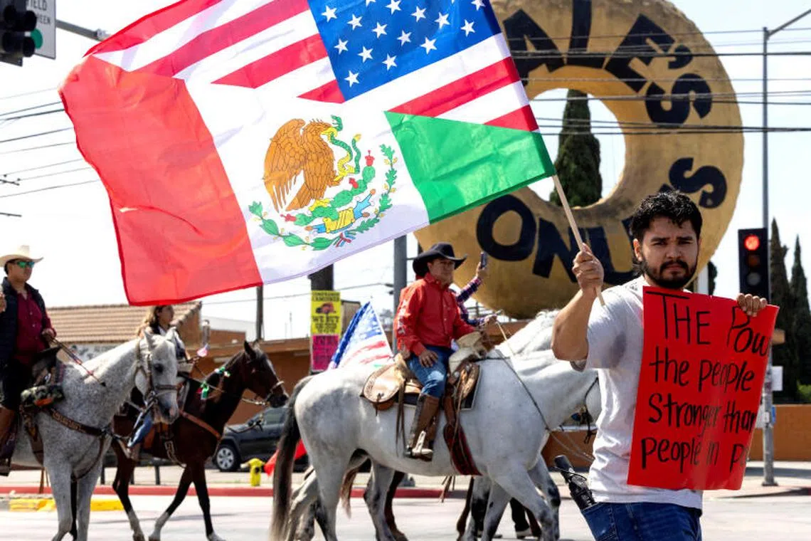 A demonstrator displays a U.S.-Mexican flag and a sign as riders and protesters, organized by Connecting Compton, take part in a 'cabalgata' for human rights following multiple detentions by Immigration and Customs Enforcement (ICE), in the Los Angeles County city of Compton, California, U.S., June 22, 2025. REUTERS/Jill Connelly