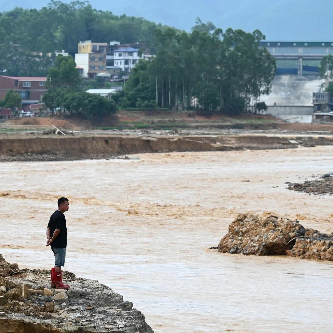 TOPSHOT - A man looks at water flowing from the collapsed Liulan reservoir in Liulan village in Hengzhou city, Chinas southwest Guangxi region, on July 8, 2026. Rescuers scoured flooded parts of China for survivors on July 8 after storms killed 17 people and caused dozens of rivers to overflow and a reservoir dam to burst, with officials warning of more rain. (Photo by GREG BAKER / AFP)