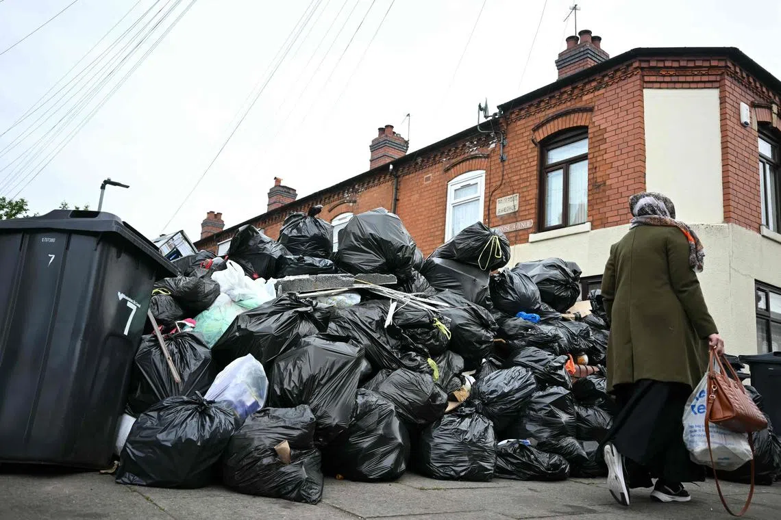 A resident walks past uncollected bin bags piled up on Poplar Road in Birmingham, central England, on April 15, 2025. Residents are desperately trying to get rid of an estimated 17,000 tonnes of trash that has piled up since refuse workers ramped up a strike last month. Four weeks in, the city council has declared a "major incident," the prime minister has had to defend the government's response in parliament, and residents say their problems are worsening by the day. (Photo by Paul ELLIS / AFP)