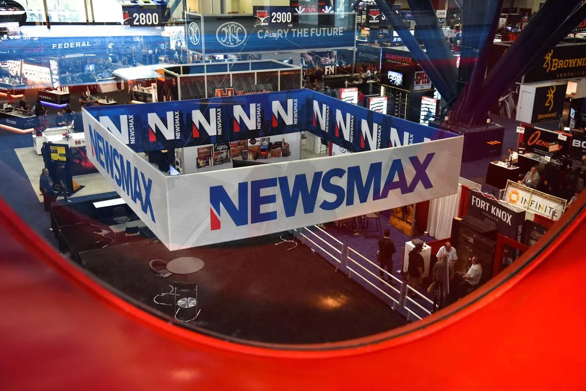 FILE PHOTO: A Newsmax booth broadcasts as attendees try out the guns on display at the National Rifle Association (NRA) annual convention in Houston, Texas, U.S. May 29, 2022. Picture taken through glass. REUTERS/Callaghan O'Hare/File Photo
