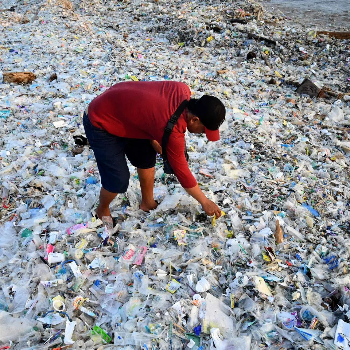 TOPSHOT - A man looks through plastic and other debris washed ashore at Kedonganan Beach near Denpasar on Indonesia's resort island of Bali on March 19, 2024. (Photo by SONNY TUMBELAKA / AFP)