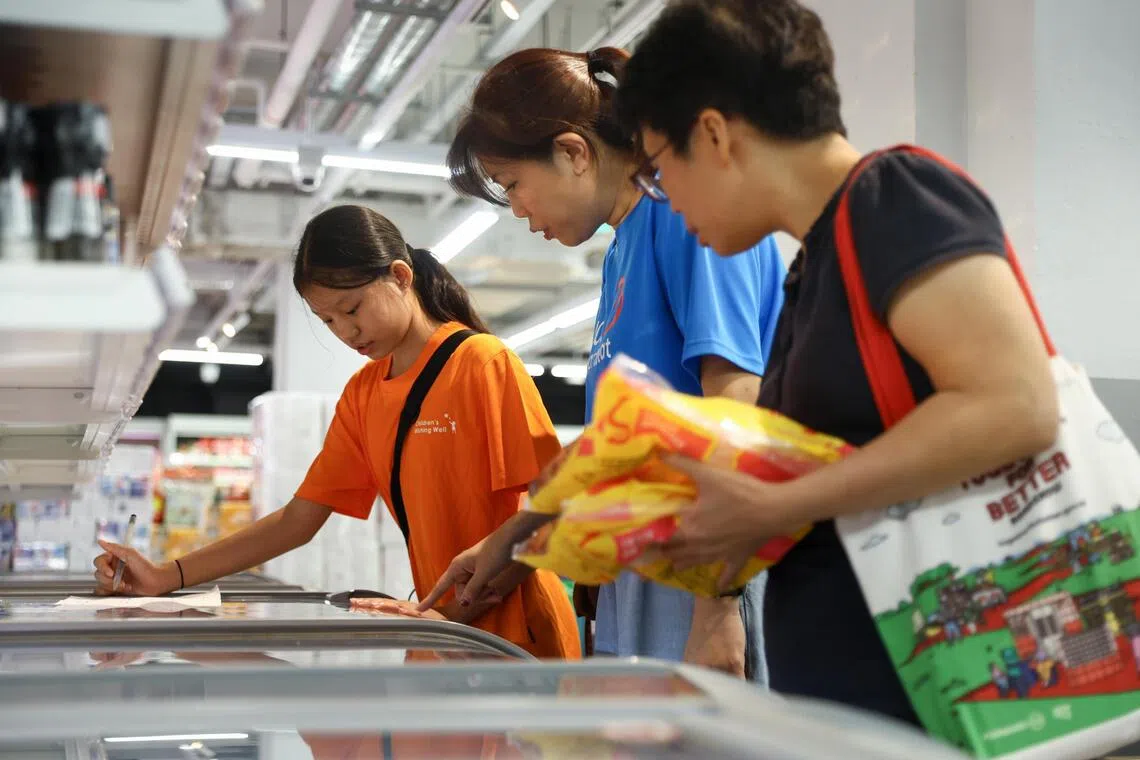 (From left) Najwa Chua Ai Xin, 12, UOB Heartbeat volunteer Ho Ying Ying and ST reporter Chor Khieng Yuit searching for frozen food on Najwa’s grocery list during a July 22 shopping run.