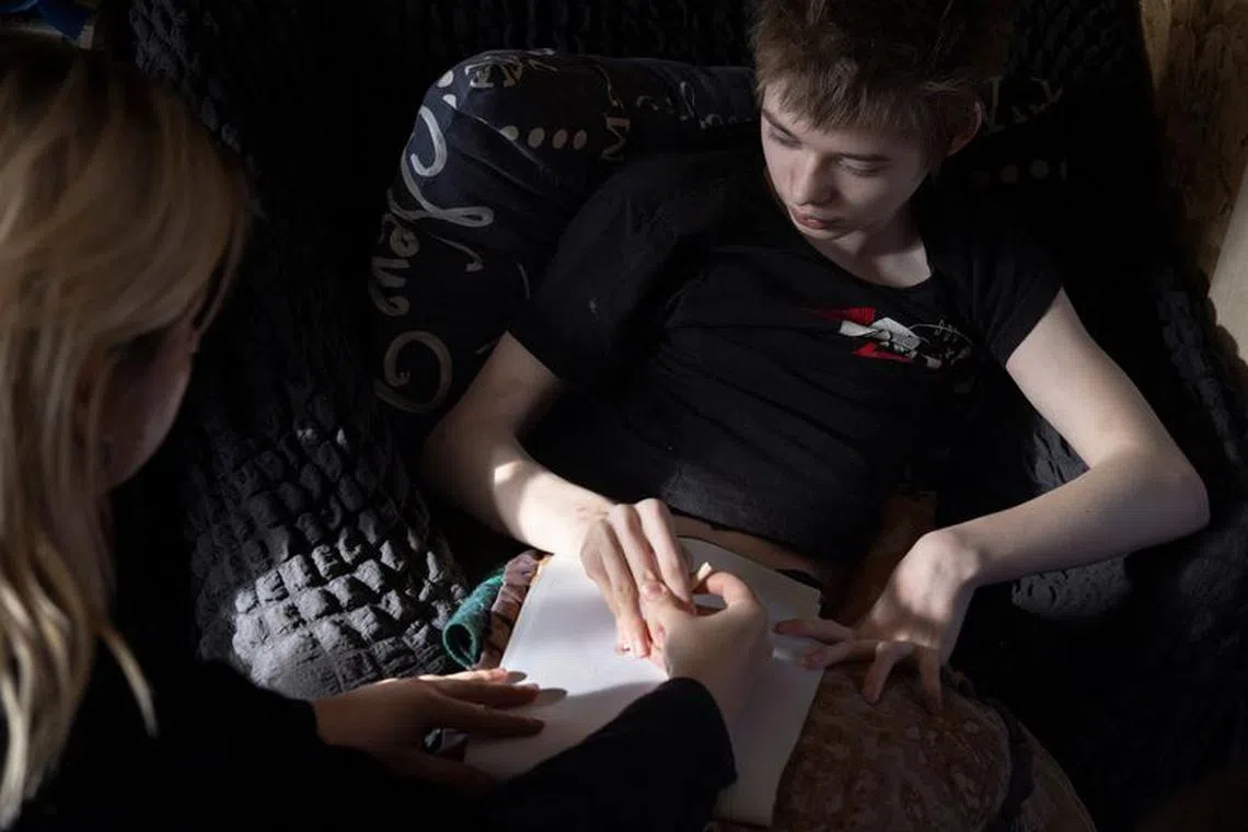 Svitlana Korzun of the Base UA volunteer organisation assists 16-year-old Ivan, who is living with cerebral palsy, during a drawing exercise at his home, amid Russia’s attack on Ukraine, in the village of Tetianivka, Ukraine, January 31, 2024.  REUTERS/Thomas Peter
