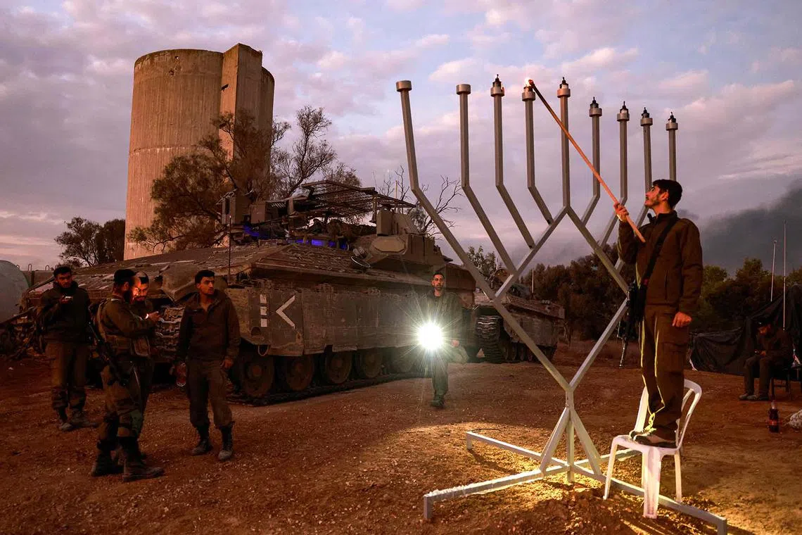 An Israeli soldier lights the sixth candle of the sixth day of the Jewish Hanukkah holiday at a position near the Gaza border on December 12, 2023, amid continuing battles between Israel and the militant group Hamas. (Photo by Menahem Kahana / AFP)