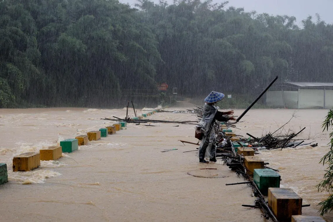 A villager clears tree branches stuck on the bridge in the rain at a flooded area in Liuzhou, in south=western China's Guangxi province on June 13.