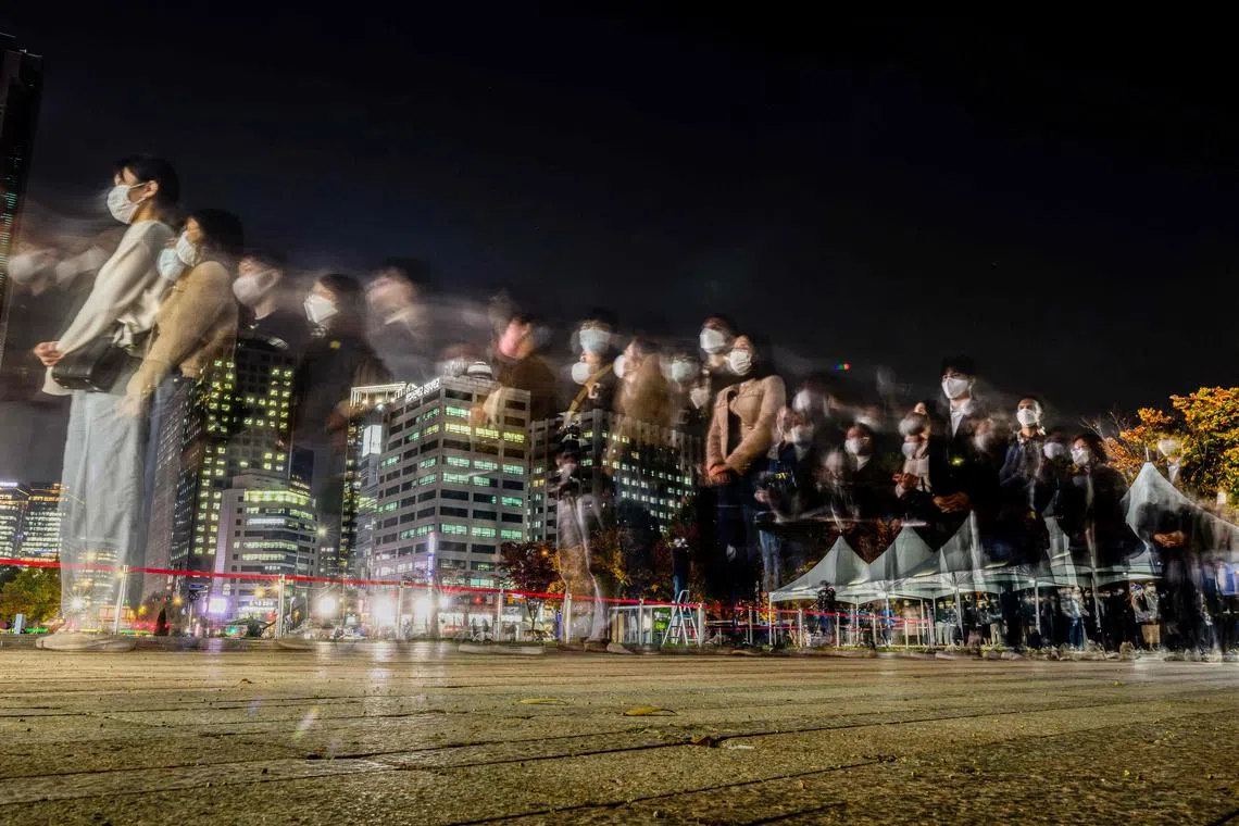 A slow shutter photo showing mourners standing in line to write in a book of remembrance, after paying tribute in front of a joint memorial altar for victims of the deadly Halloween crowd crush, outside the City Hall in Seoul on Nov 1, 2022.