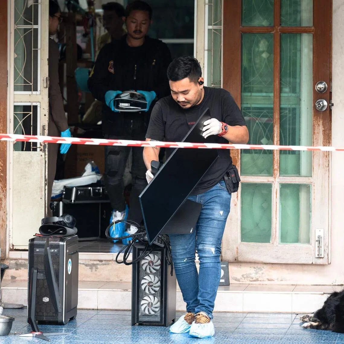 Officials carry a computer out of the house where a teenage suspect is suspected of killing his grandparents before carrying out a school shooting in Nonthaburi province.